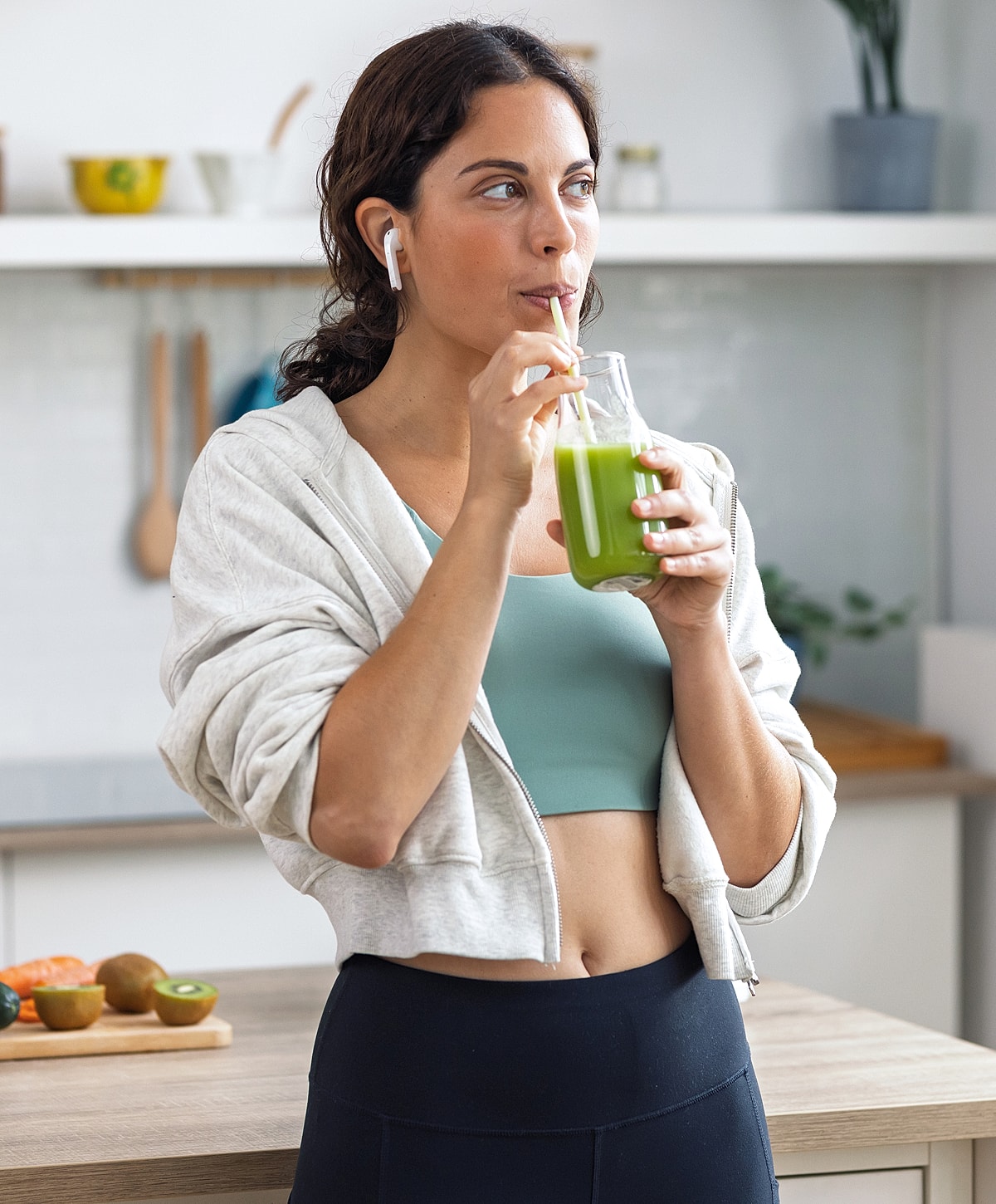 Woman sipping green juice in kitchen.