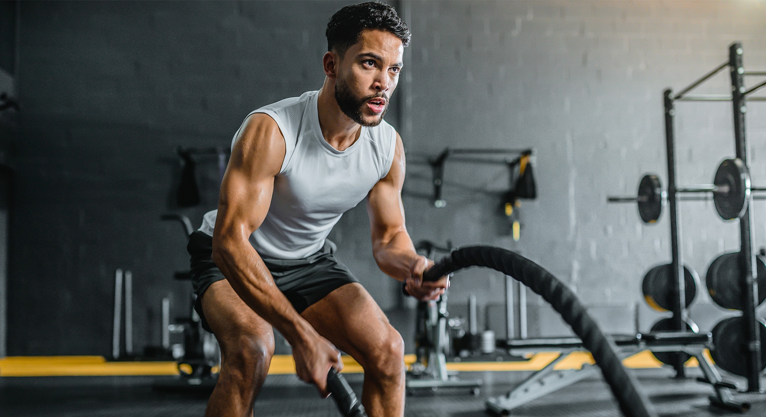 Man exercising with battle ropes in gym.