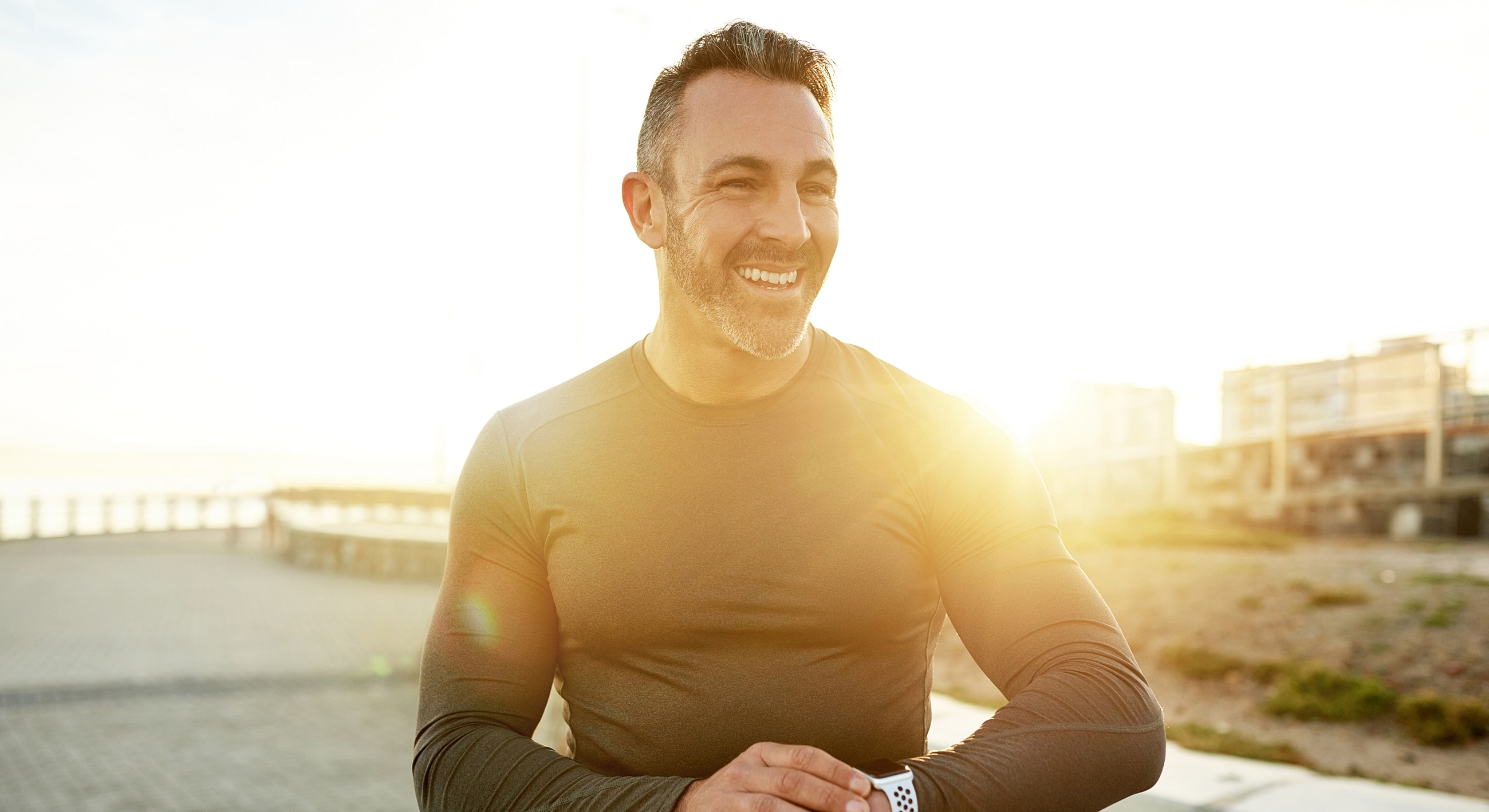 Smiling man enjoying sunset outdoors in workout attire.